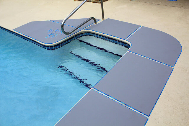 Grey faux teak SeaDek for pool deck, highlighting wet traction grooves and contrasting blue inlay by the water