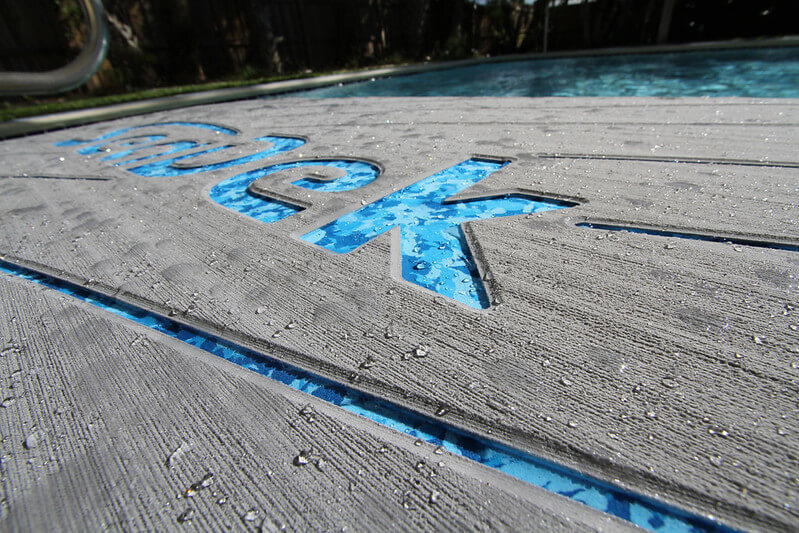 Textured SeaDek pool safety mats with water beading on the surface next to a clear blue pool