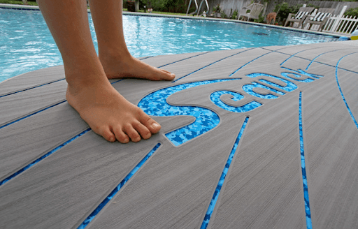 Close-up of grey SeaDek non-slip pool deck mats with water droplets beside a blue swimming pool